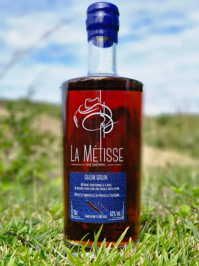Bouteille La Métisse rhum brun au gaïac devant les collines calédoniennes